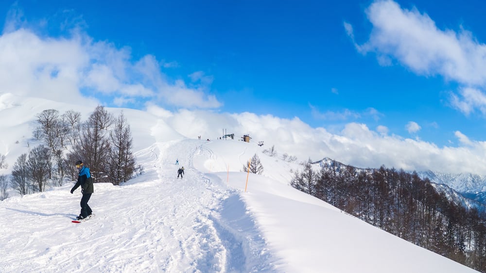 A snowy mountain slope with skiers and a clear blue sky.