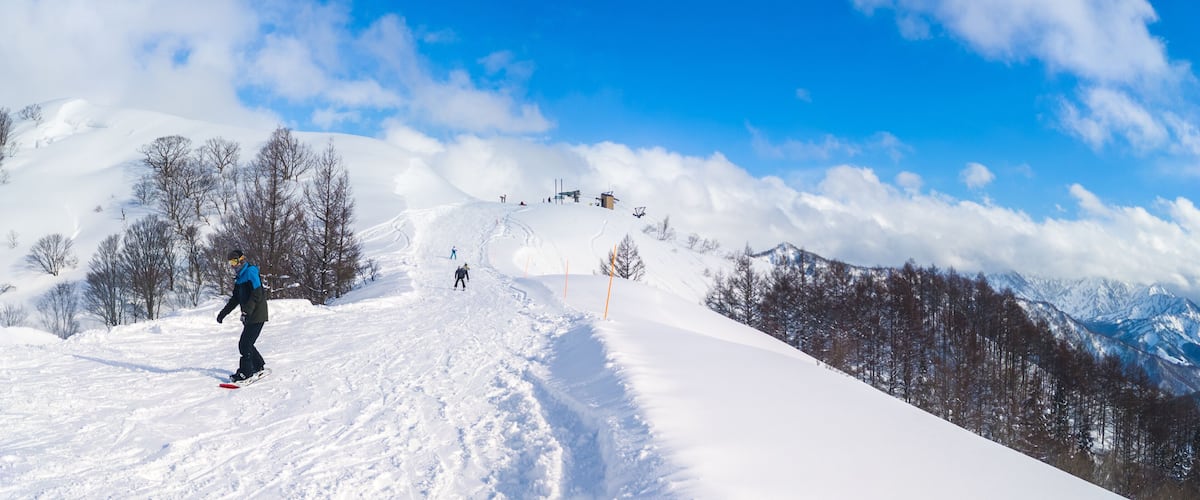 A snowy mountain slope with skiers and a clear blue sky.