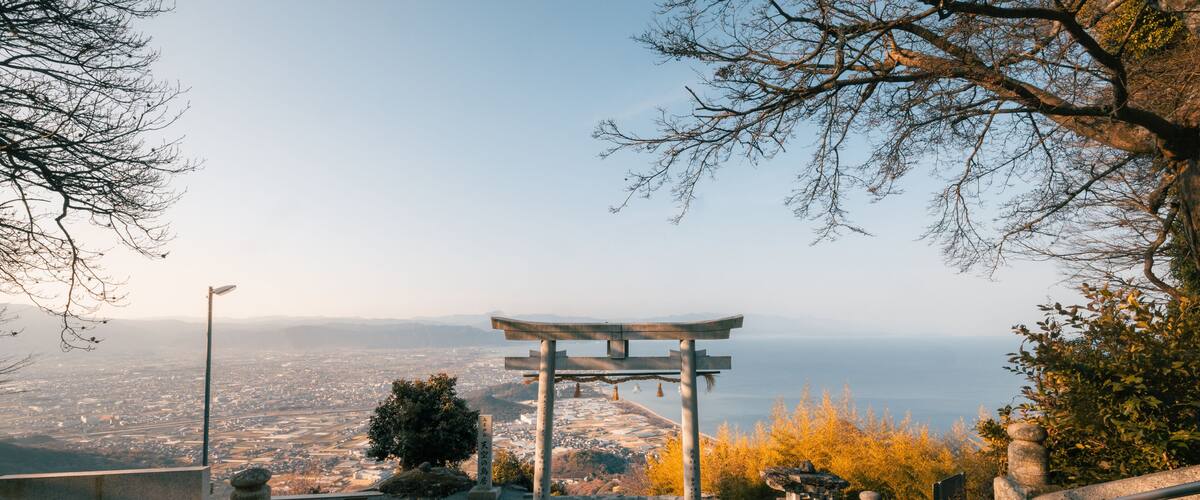 A traditional Japanese torii gate at the top of a hill overlooking a cityscape.