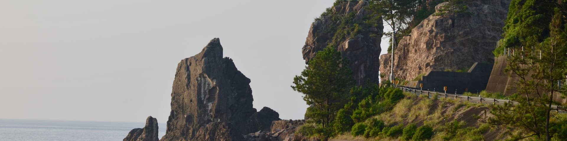 A rocky coastline with prominent rock formations and a concrete barrier.