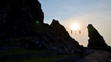 Pôr do sol sobre falésias rochosas com uma ponte suspensa.