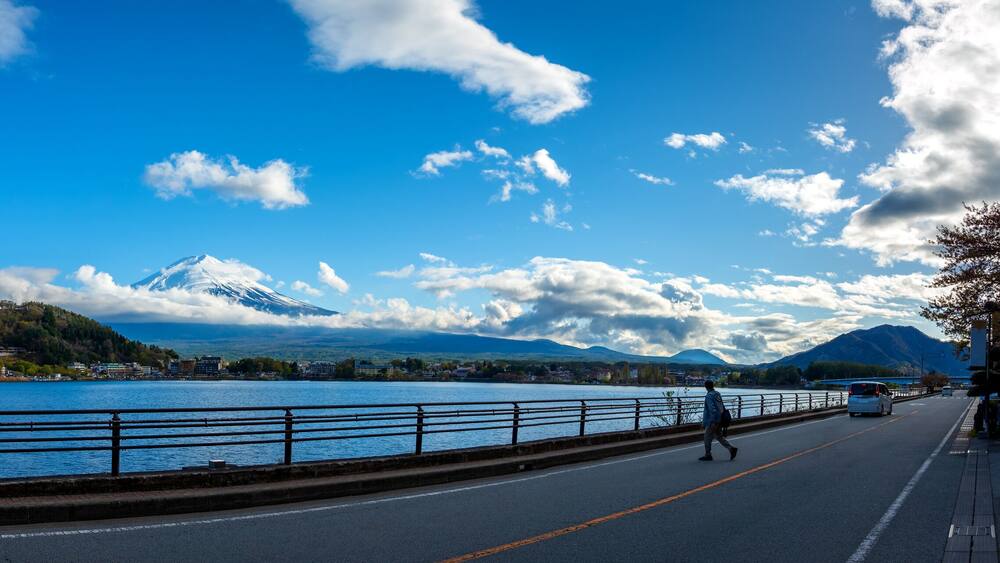 A lake with a mountain in the background, a road with a pedestrian, and a clear blue sky.
