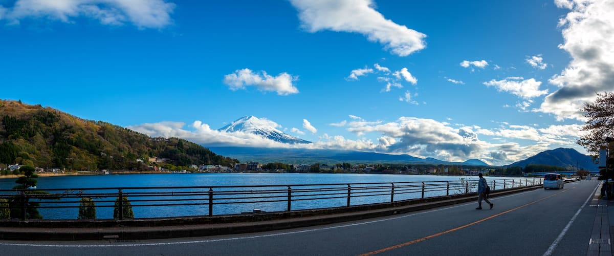 A lake with a mountain in the background, a road with a pedestrian, and a clear blue sky.