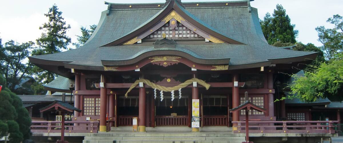 A traditional Japanese temple with a curved roof, red columns, and a stone pathway leading to the entrance.