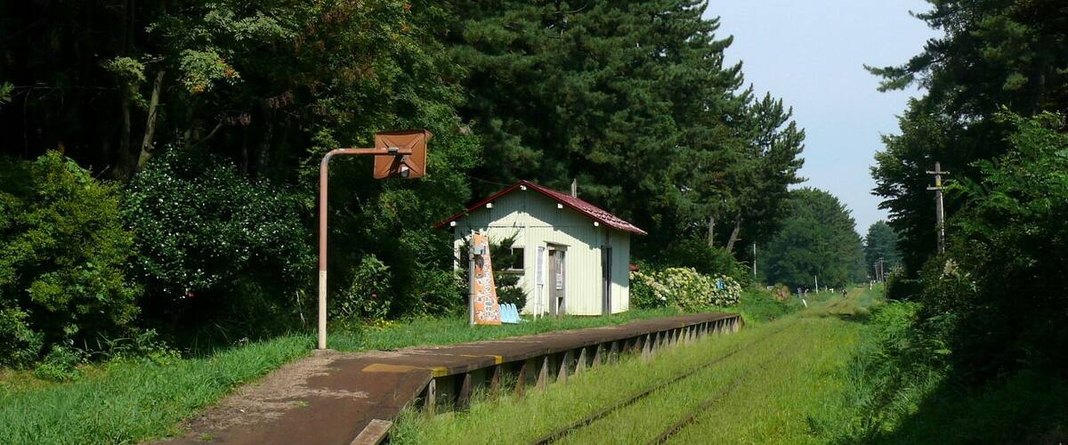 A rural railway station with a small building, tracks, and surrounding greenery.