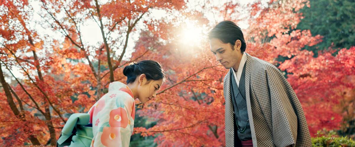 Two people in traditional attire standing in a garden with red foliage.