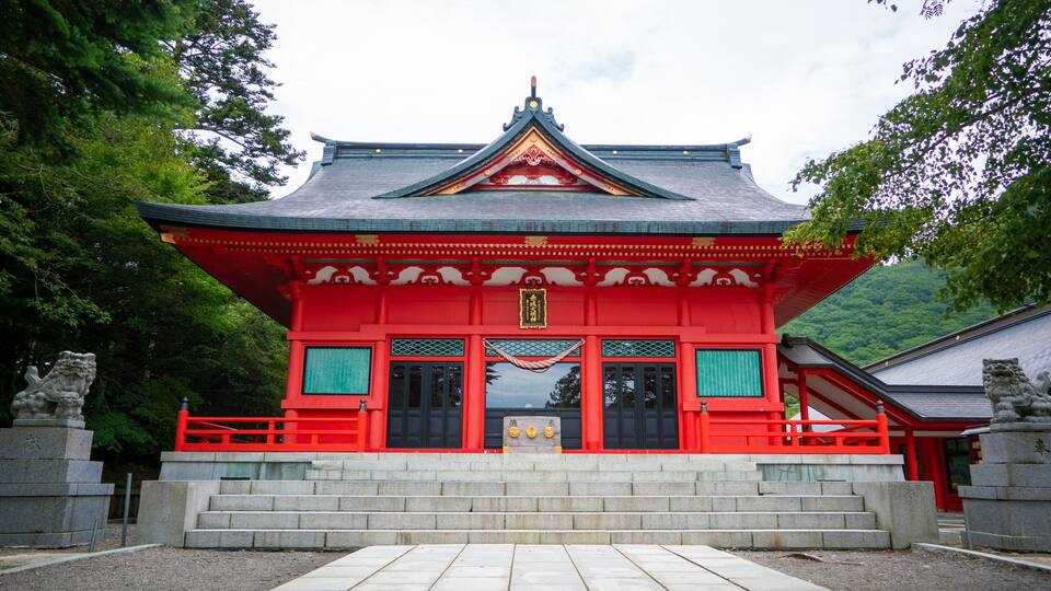 A traditional Japanese temple with a red roof and grey walls, surrounded by trees.
