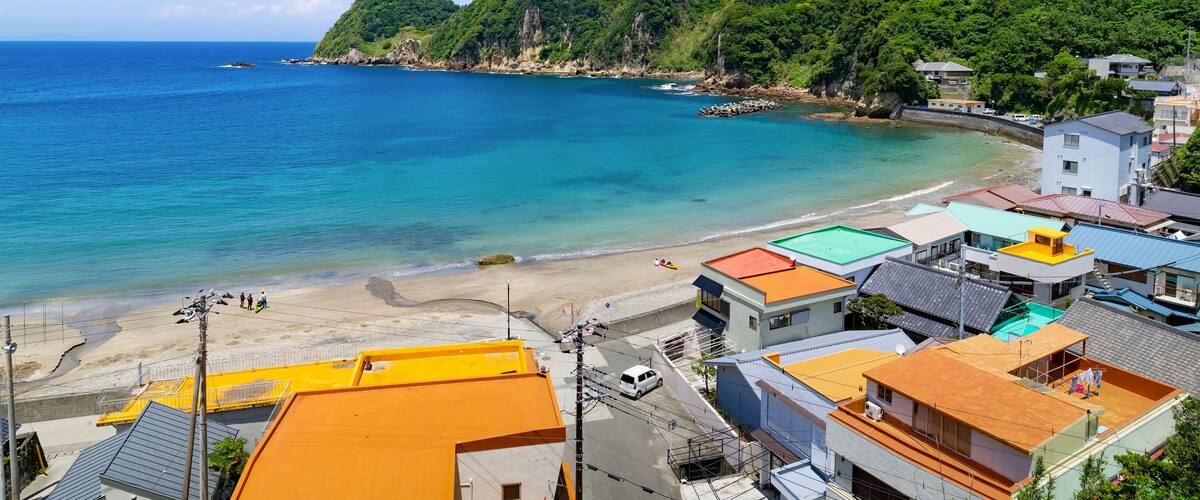 A coastal town with a beach, houses, and a mountain.