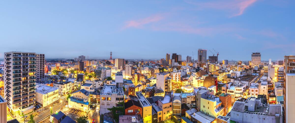 A cityscape at dusk with illuminated buildings and a clear sky.