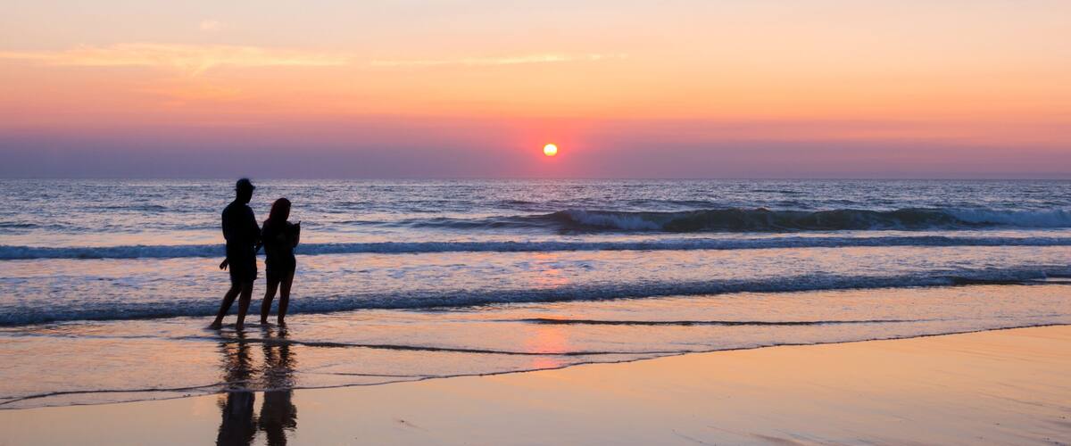 A sunset over the ocean with two silhouetted figures on the beach.