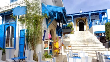 A blue and white building with a staircase leading to a door, surrounded by white wicker chairs and tables.