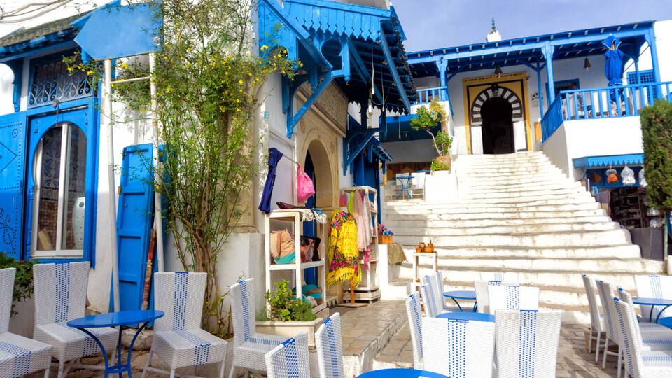 A blue and white building with a staircase leading to a door, surrounded by white wicker chairs and tables.