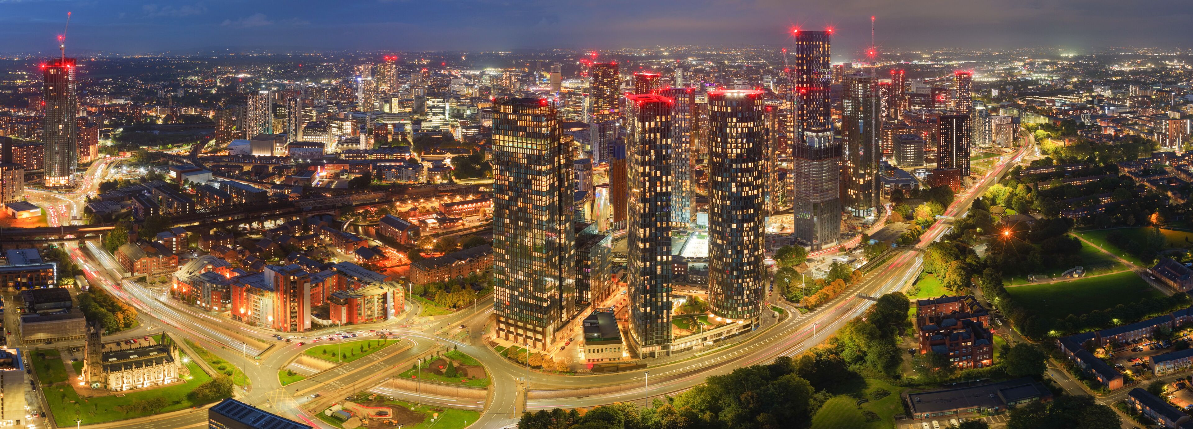 Striking long-exposure night panorama of Manchester skyline with glowing city lights and traffic along Mancunian Way.