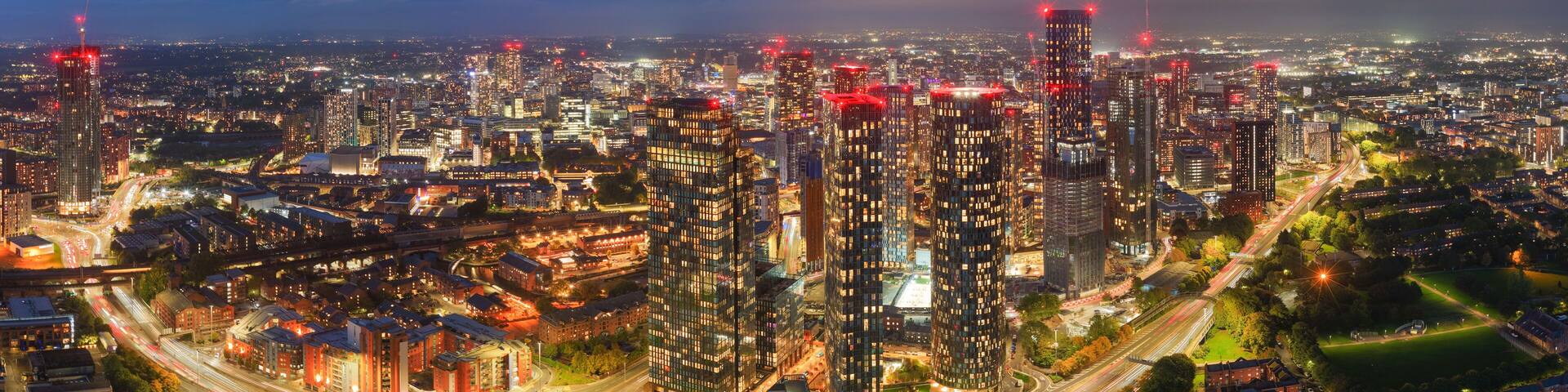 Striking long-exposure night panorama of Manchester skyline with glowing city lights and traffic along Mancunian Way.