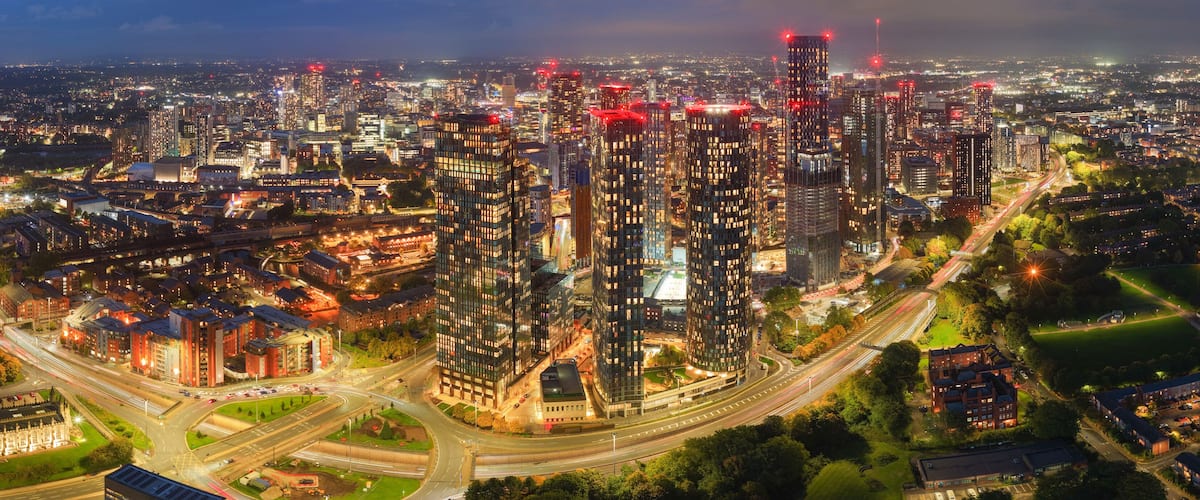 A cityscape at night with illuminated skyscrapers, a highway, and surrounding greenery.