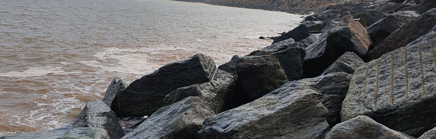 A rocky shoreline with waves crashing against the rocks and a distant cliff.