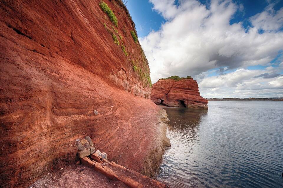 Une falaise de roche rouge, avec une petite cascade et une étendue d’eau calme.