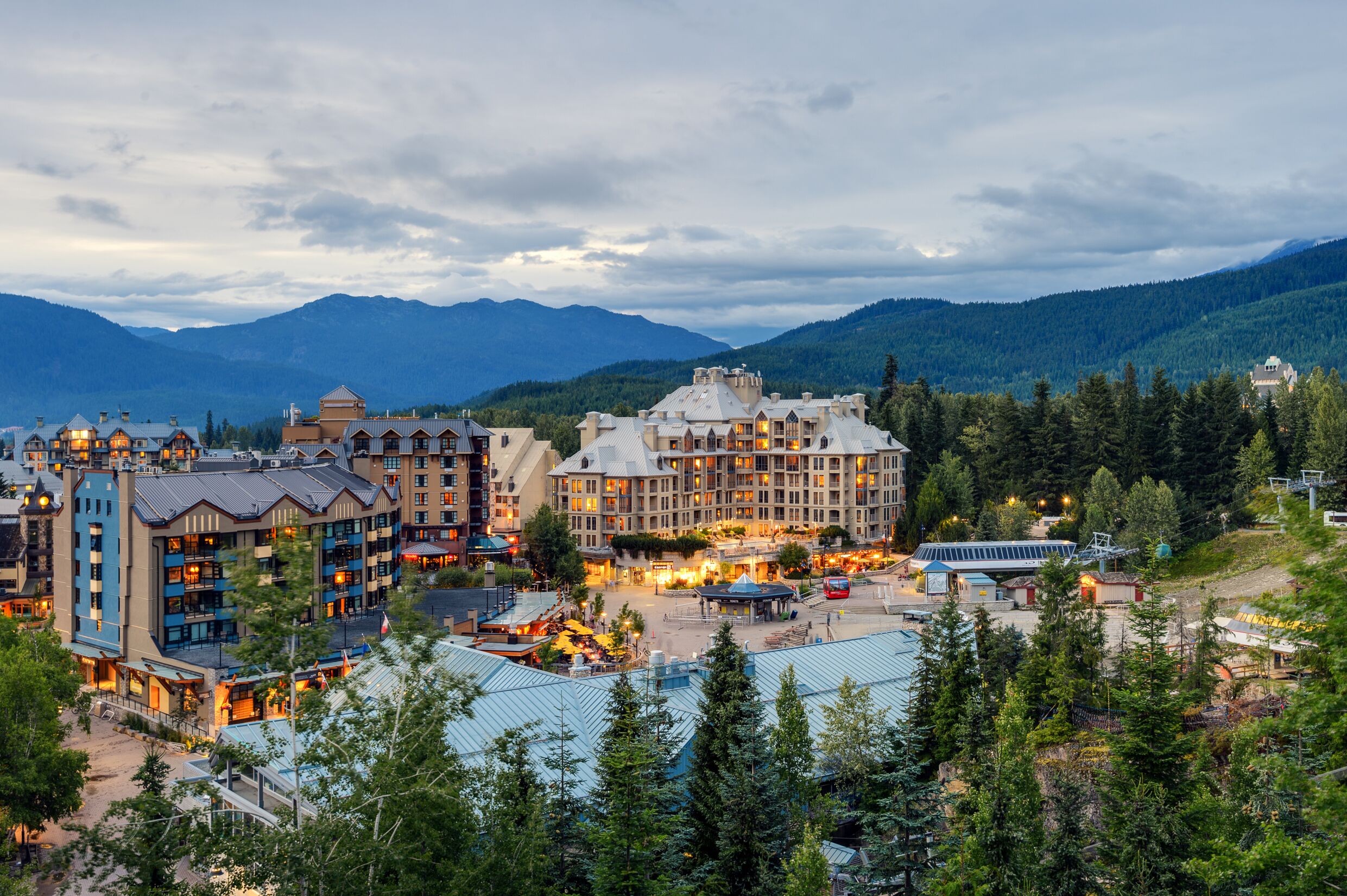 A resort town with multiple buildings, a ski lift, and mountains in the background.