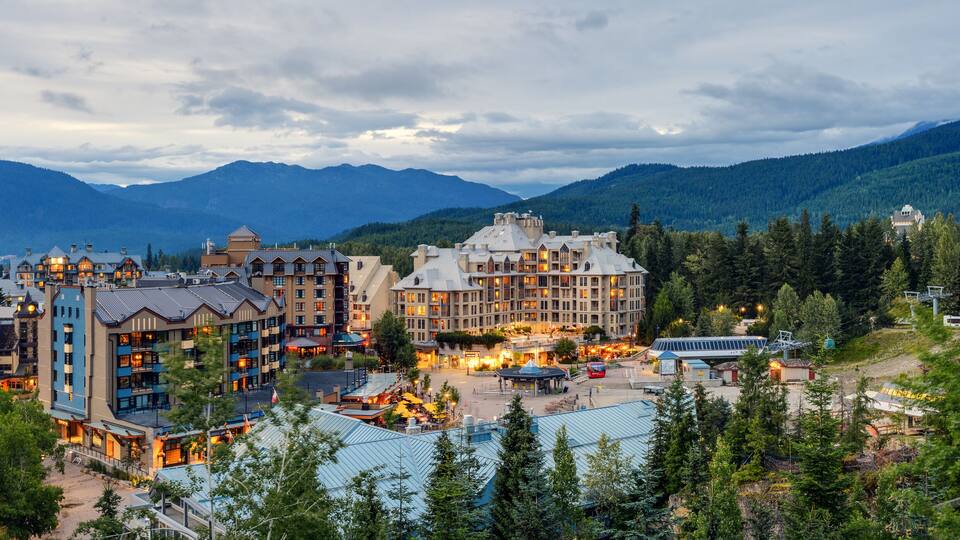 A resort town with multiple buildings, a ski lift, and mountains in the background.
