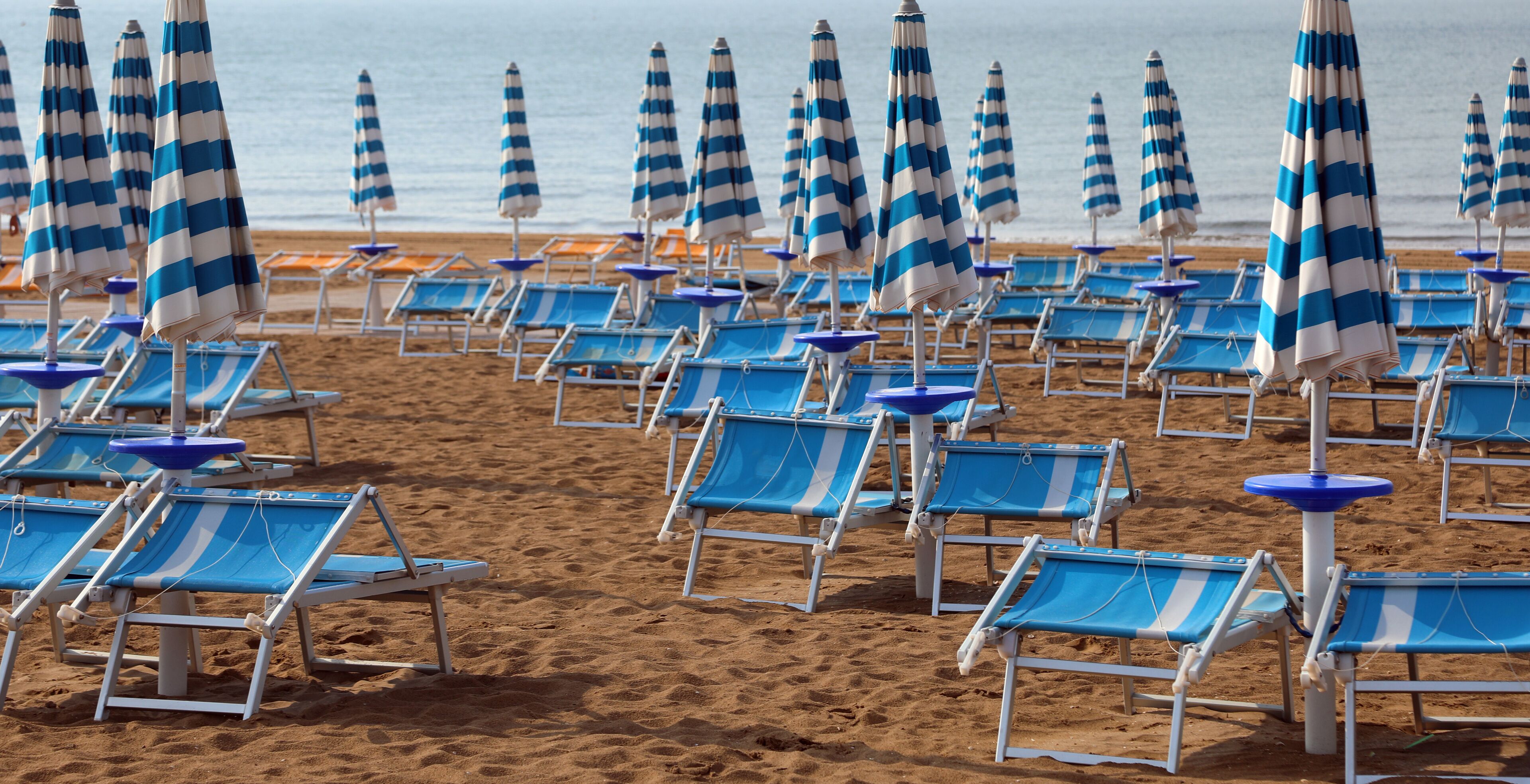 A beach with rows of blue and white striped beach umbrellas and matching lounge chairs.