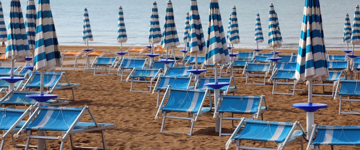 A beach with rows of blue and white striped beach umbrellas and matching lounge chairs.