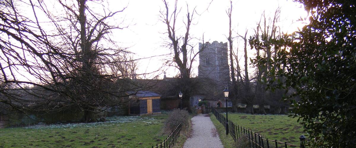 A gravel path leading to a stone tower, surrounded by trees and a grassy field.