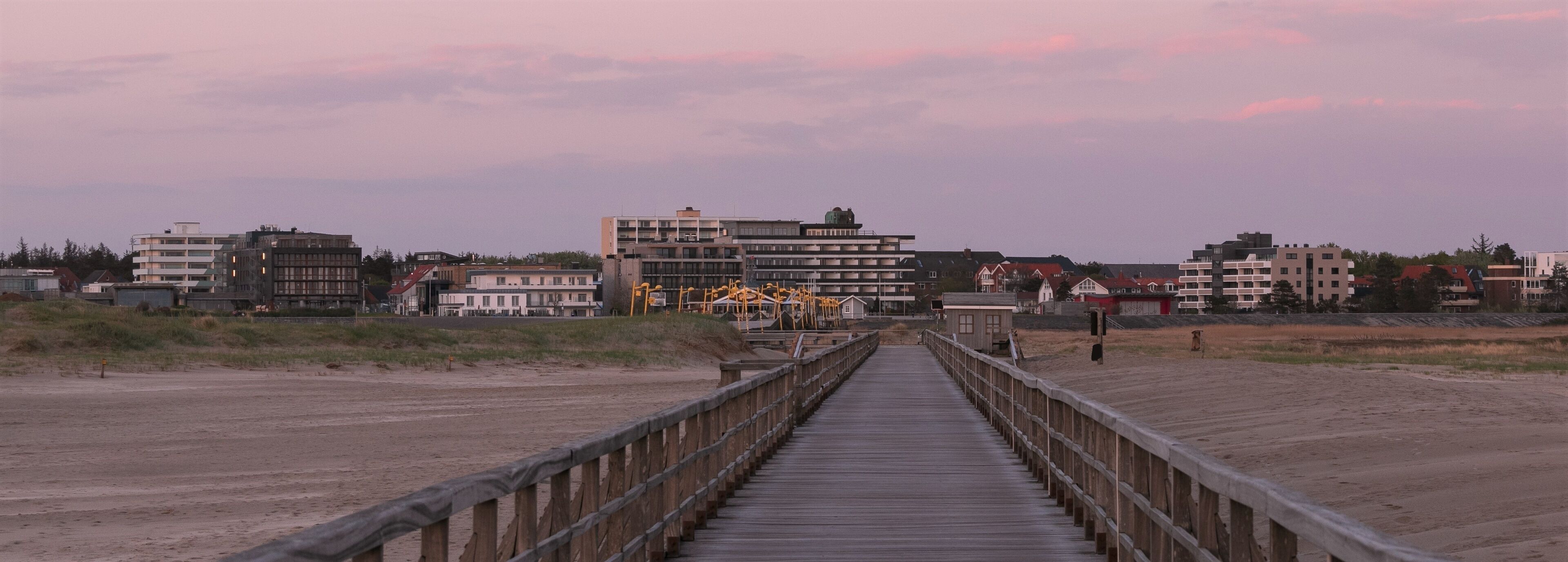 A wooden boardwalk leading to buildings and a beach.