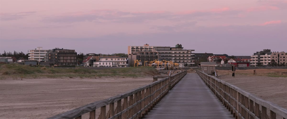 A wooden boardwalk leading to buildings and a beach.