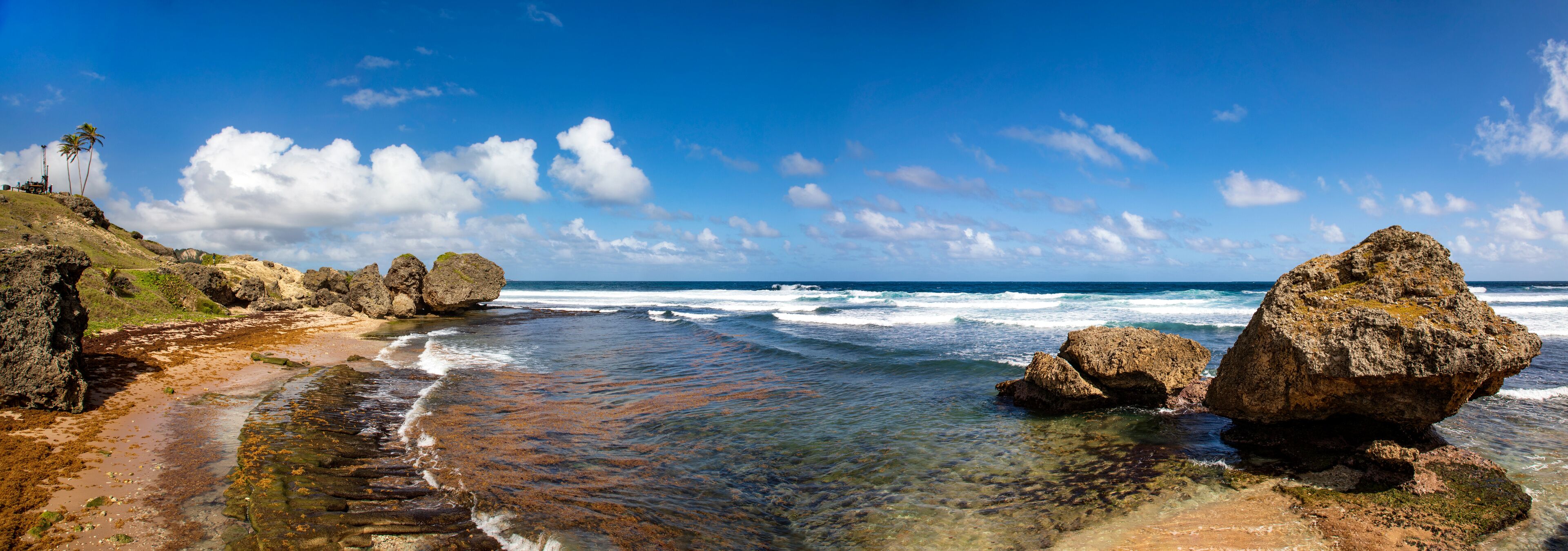 A rocky beach with clear water, large boulders, and a clear sky.