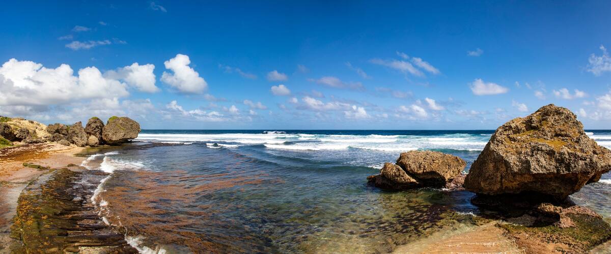 A rocky beach with clear water, large boulders, and a clear sky.