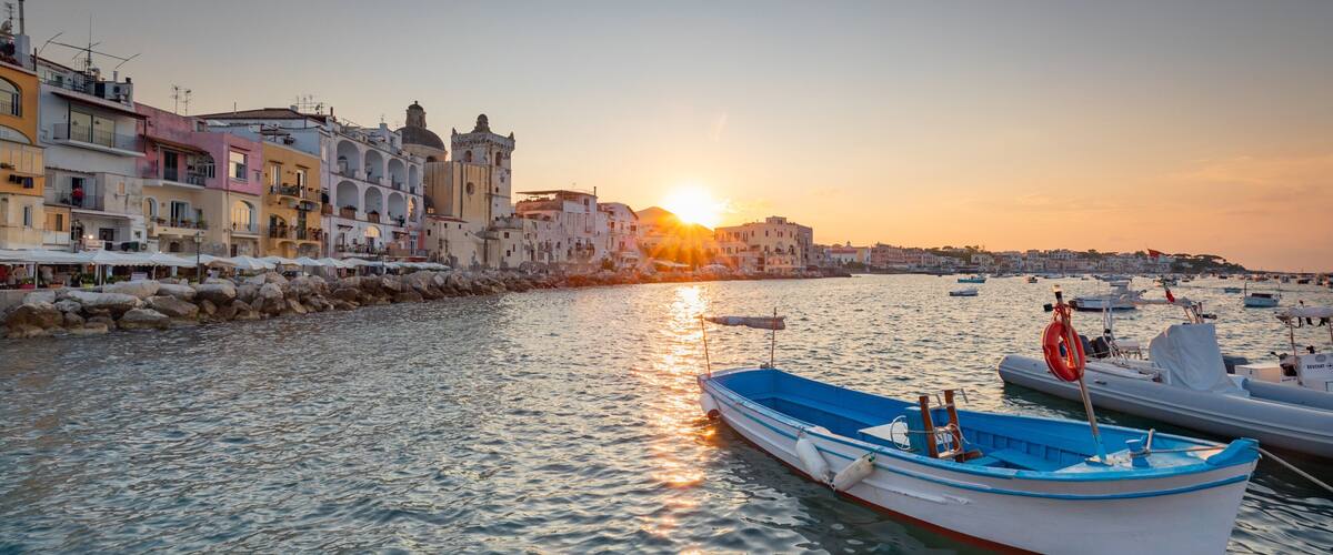 A coastal town with colorful buildings, a calm sea, and boats docked at the harbor during sunset.