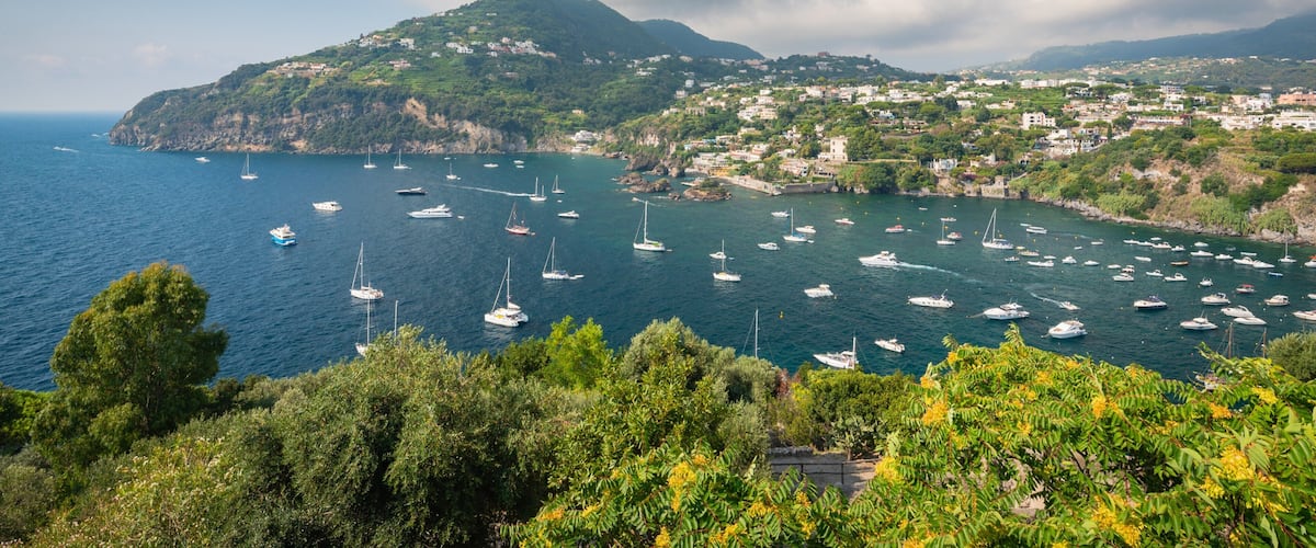 A coastal town with boats anchored in the bay, surrounded by lush greenery and hills.