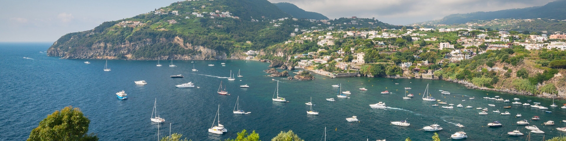 A coastal town with boats anchored in the bay, surrounded by lush greenery and hills.
