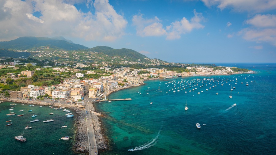 Un pueblo costero con un muelle, barcos y montañas al fondo.