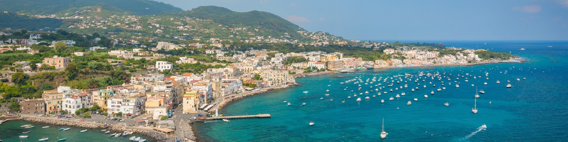Un pueblo costero con un muelle, barcos y montañas al fondo.