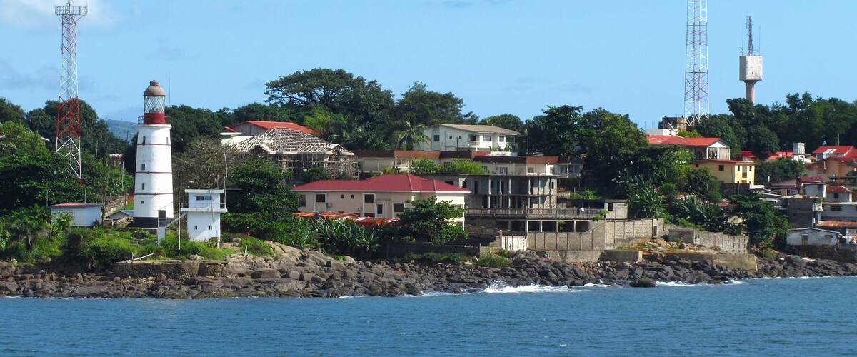 A coastal town with a prominent lighthouse, residential buildings, and rocky shoreline.