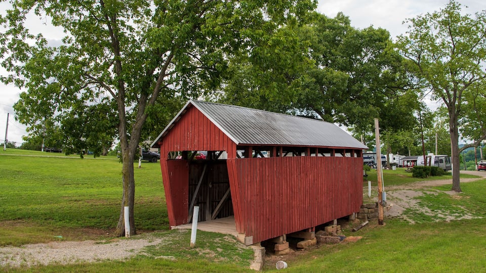 A red wooden structure with a metal roof, surrounded by green grass and trees.