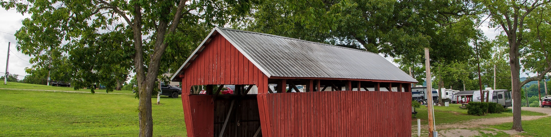 A red wooden structure with a metal roof, surrounded by green grass and trees.