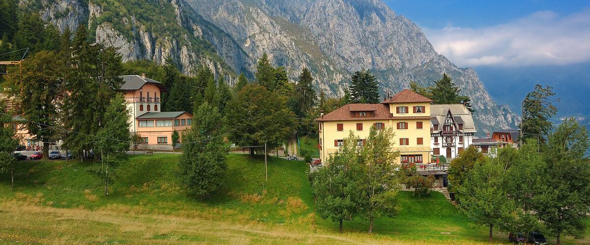 A mountain village with houses on a hillside, surrounded by lush greenery and dramatic mountain peaks.
