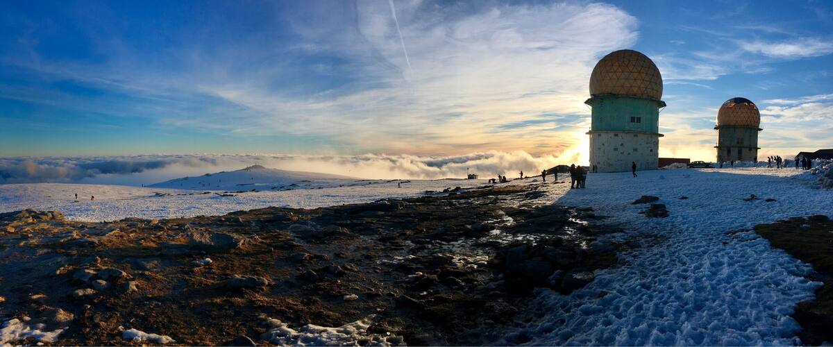 A snowy landscape with two large domed structures, likely radar stations, and a clear sky with clouds.