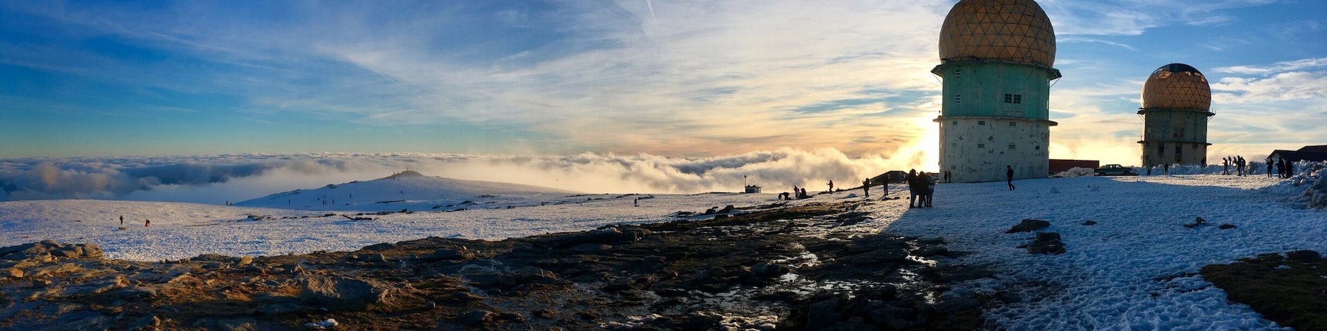 A snowy landscape with two large domed structures, likely radar stations, and a clear sky with clouds.
