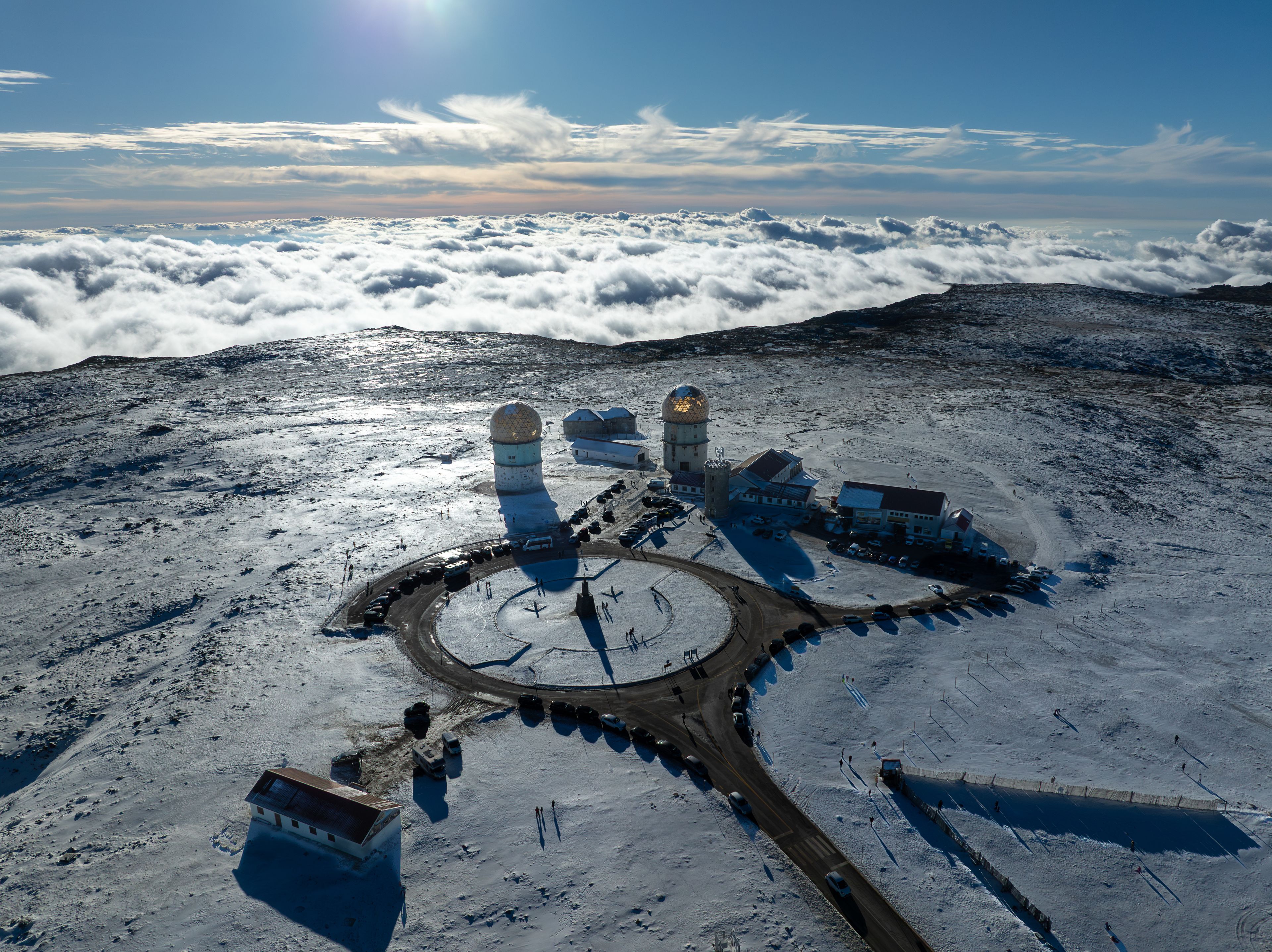 Aerial view of the Torre da Serra da Estrela observatory domes on a snowy mountain peak above a sea of clouds in Unhais da Serra, Castelo Branco, Portugal.