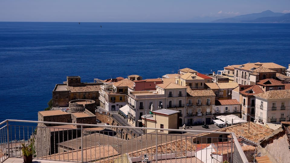 A coastal town with terracotta-roofed buildings and a clear blue sea.