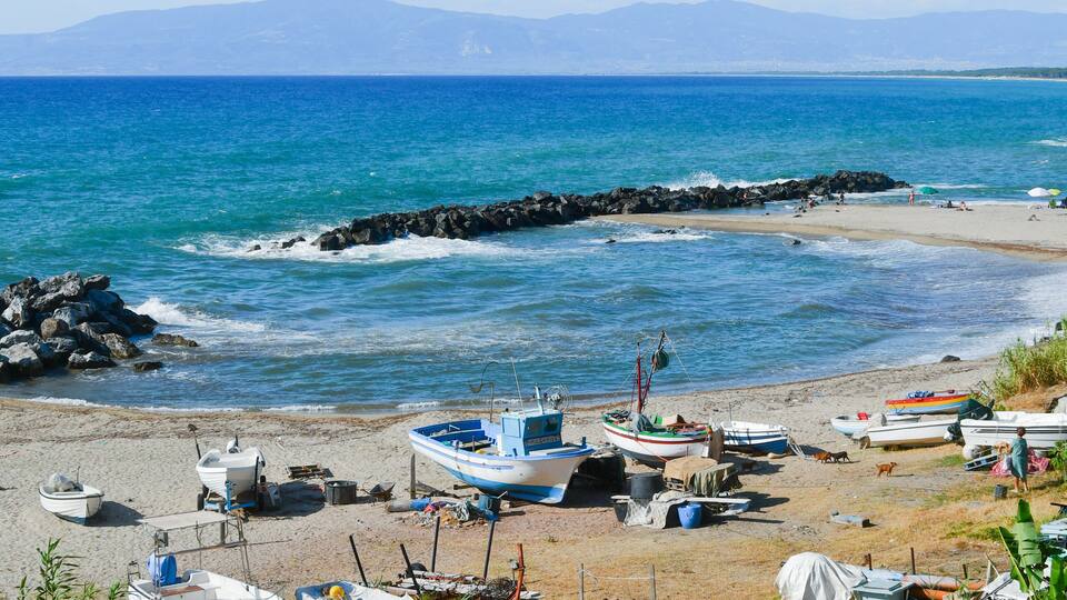 A beach with boats, rocky breakwaters, and a clear blue sea.