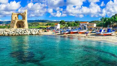 A coastal town with a historic stone structure, boats, and a clear blue sea.