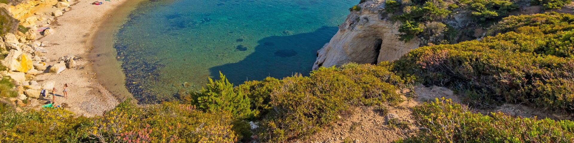 A coastal landscape with a clear beach, rocky cliffs, and a distant town.