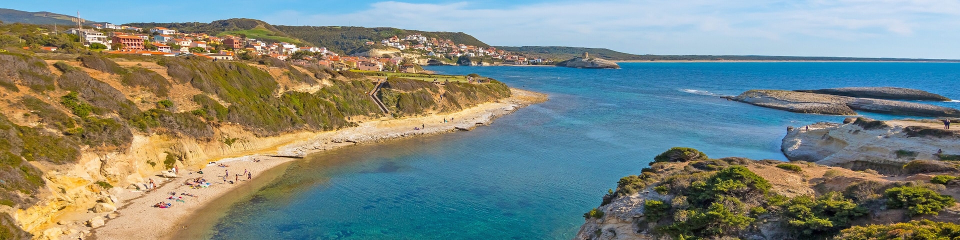 Un paysage côtier avec une plage de sable fin, des falaises rocheuses et une ville située au loin.