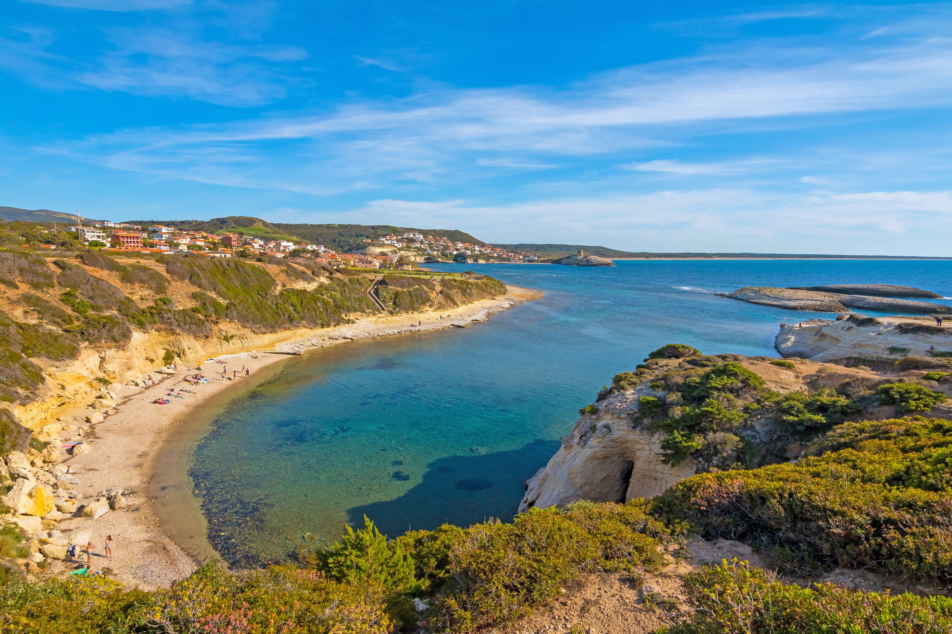 A coastal landscape with a clear beach, rocky cliffs, and a distant town.