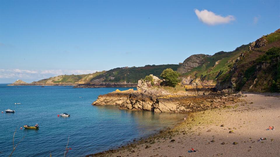 A coastal landscape with rocky cliffs, a sandy beach, and calm blue waters with boats.