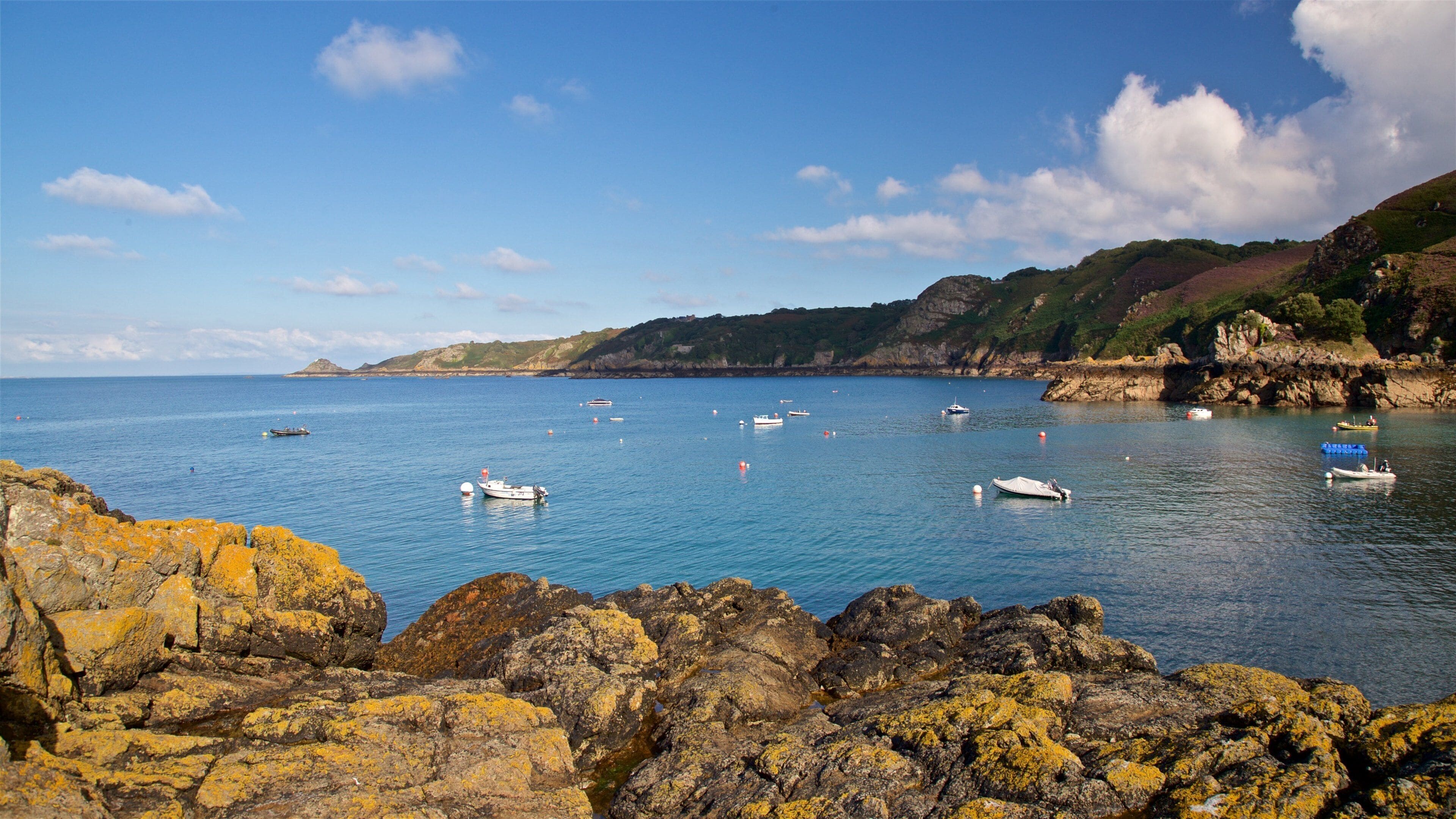 A coastal scene with rocky shores, calm sea, and several boats.